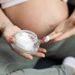 Ciężarna kobieta nakłada krem na palec z otwartego słoiczka.
