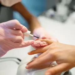 Stylistka w różowych rękawiczkach pokazuje, jak nakładać żel budujący na paznokieć.