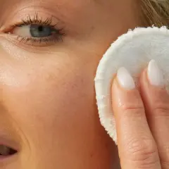 Delikatny peeling na prosaki, który odświeża skórę. Kobieta z blond włosami i niebieskimi oczami stosuje go na twarz.