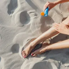 Kobieta smaruje nogi kremem z filtrem zawierającym ethylhexyl methoxycinnamate na piaszczystej plaży.