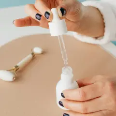 Kropla niacynamidu z pipetki wpada do białej buteleczki. Obok leży jadeitowy roller.