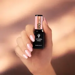Dłoń z różowymi paznokciami trzyma buteleczkę Liquid Poly Gel Victoria Vynn. To produkt do stylizacji paznokci.