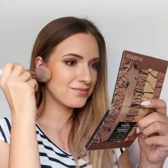 Kobieta nakłada puder pędzlem, trzymając w dłoni paletkę do konturowania. Efekt subtelnego makijażu no makeup.
