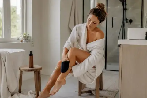 Kobieta w szlafroku aplikuje samoopalacz na nogi. Zastanawiasz się, po jakim czasie zmyć samoopalacz, by uzyskać idealny odcień?