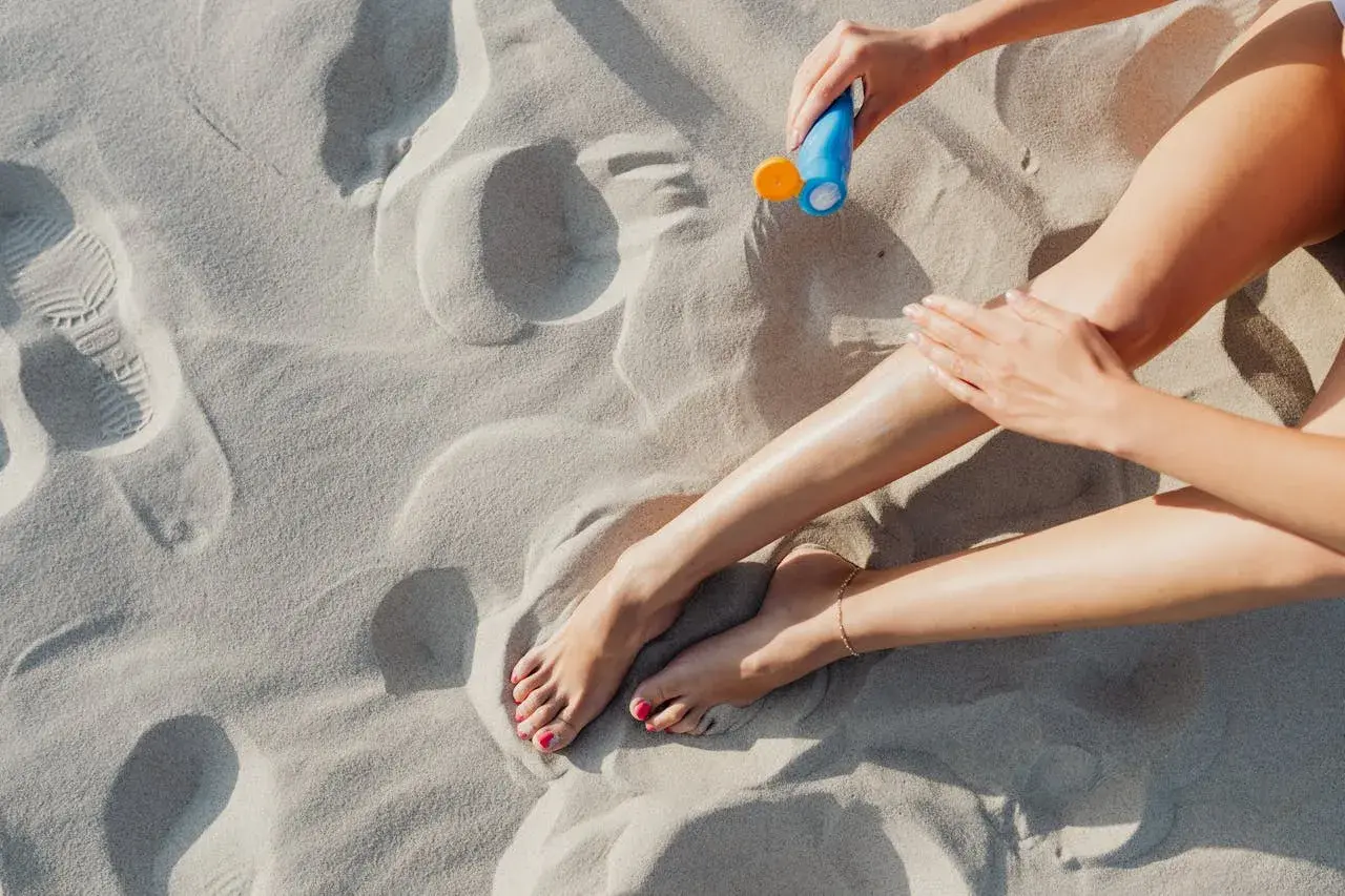 Kobieta smaruje nogi kremem z filtrem zawierającym ethylhexyl methoxycinnamate na piaszczystej plaży.