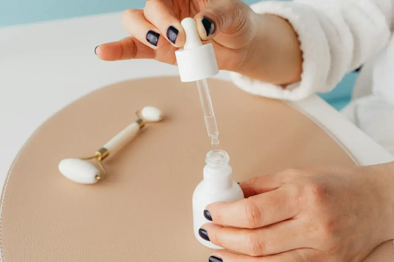 Kropla niacynamidu z pipetki wpada do białej buteleczki. Obok leży jadeitowy roller.